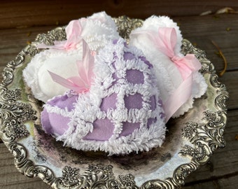 May include: Three heart-shaped pillows with white trim and pink ribbon bows. The pillows are on a silver tray with an ornate design.