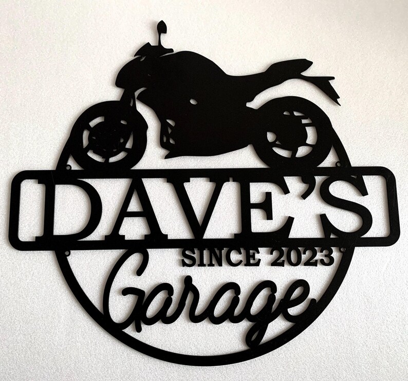 K&ouml;nnte beinhalten: Schwarzes Metallschild mit einer Motorradsilhouette, dem Text "Dave's Garage Since 2023" und einem runden Rand.