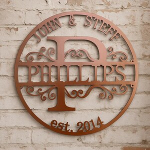 May include: A copper-colored metal family name sign. The sign is circular with the names "JOHN & STEFF" at the top and "PHILLIPS" in the center. The letter "D" and a tree-like design are incorporated. The year "est. 2014" is at the bottom.
