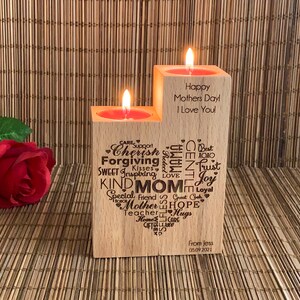 May include: Two wooden candle holders with a heart-shaped design and words like "Cherish", "Forgiving", "Kind Mom", "Hope", and "Trust" engraved on them. The candle holders are on a woven bamboo surface. The text on the right candle holder reads "Happy Mothers Day I Love You".