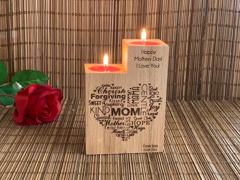 May include: Two wooden candle holders with a heart-shaped design and words like "Cherish", "Forgiving", "Kind Mom", "Hope", and "Trust" engraved on them. The candle holders are on a woven bamboo surface. The text on the right candle holder reads "Happy Mothers Day I Love You".