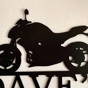 K&ouml;nnte beinhalten: Schwarze Metallsilhouette eines Motorrads mit dem Namen "DAVE'S" darunter.
