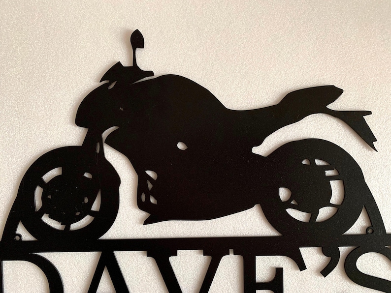 K&ouml;nnte beinhalten: Schwarze Metallsilhouette eines Motorrads mit dem Namen "DAVE'S" darunter.