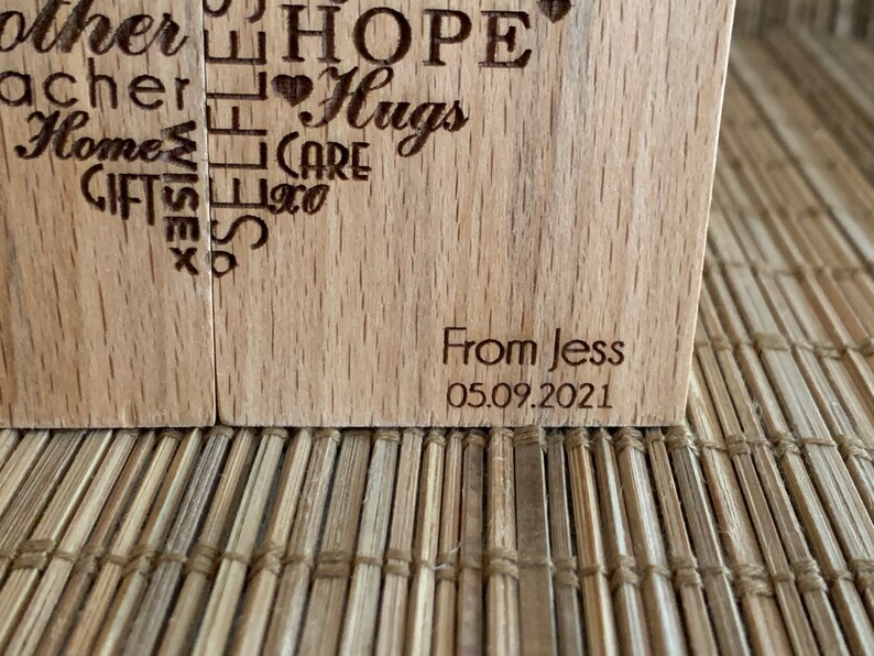 May include: Two wooden blocks with a heart shape design engraved with words like "Hope", "Hugs", "Care", "Gifts", "Home", "Teacher", "Mother", "Wise", "Love", and "From Jess 05.09.2021".