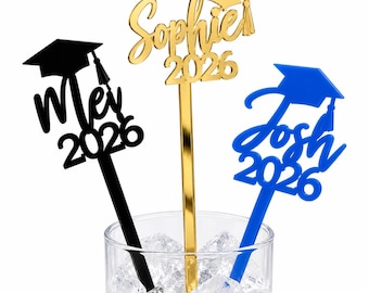 Puede incluir: Tres agitadores de bebidas personalizados para graduación con un icono de birrete y los nombres Mei, Sophie y Josh junto al año 2026. Los agitadores son de color negro, dorado y azul con un acabado brillante y tallos largos y delgados.