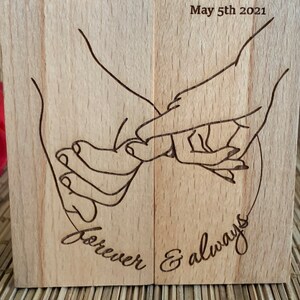 May include: A wooden block with a laser-engraved design of two hands holding each other. The text "forever & always" is engraved below the hands. The date "May 5th 2021" is engraved at the top of the block.