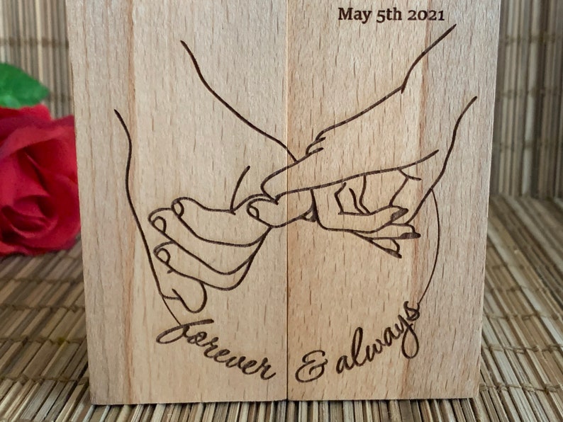 May include: A wooden block with a laser-engraved design of two hands holding each other. The text "forever & always" is engraved below the hands. The date "May 5th 2021" is engraved at the top of the block.