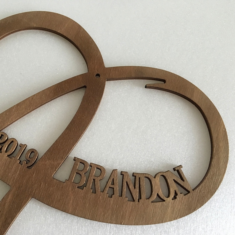 May include: A wooden heart-shaped cutout with the name "BRANDON" and the year "2019" carved into it.