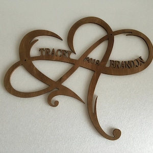 May include: A wooden heart-shaped infinity symbol with the names "Tracey" and "Brandon" and the year "2019" carved into it.