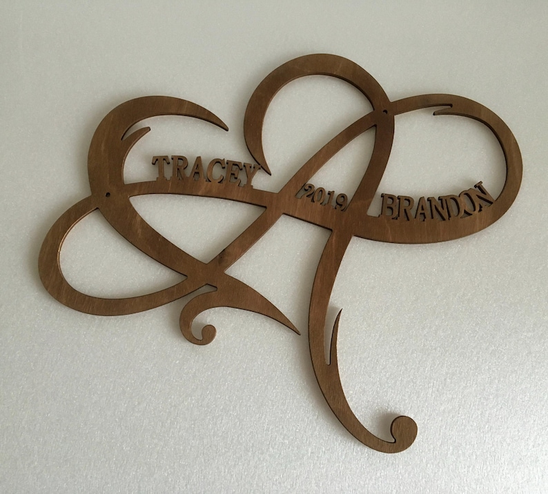 May include: A wooden heart-shaped infinity symbol with the names "Tracey" and "Brandon" and the year "2019" carved into it.