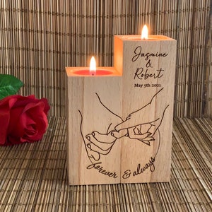 May include: Wooden candle holder with two candle wells, featuring an engraved design of two hands holding each other with the text "forever & always". The holder is personalized with the names "Jasmine & Robert" and the date "May 5th 2021".