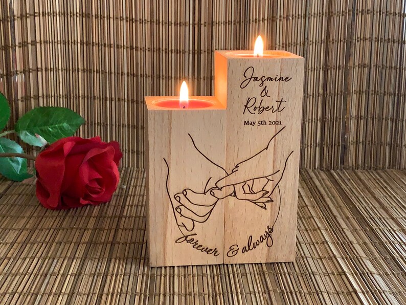 May include: Wooden candle holder with two candle wells, featuring an engraved design of two hands holding each other with the text "forever & always". The holder is personalized with the names "Jasmine & Robert" and the date "May 5th 2021".