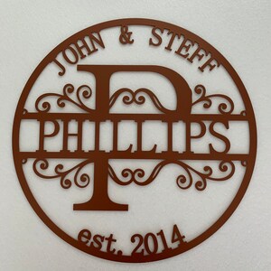 May include: A brown metal family name sign with the names "JOHN & STEFF" above "PHILLIPS" and the year "est. 2014" below. The design features a large letter "P" and decorative flourishes within a circular frame.