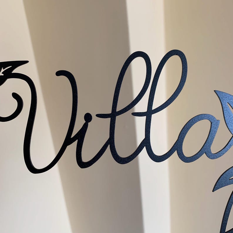 May include: Black metal sign with the word "Villa" in a cursive font. The sign has two leaf designs on either side of the word.