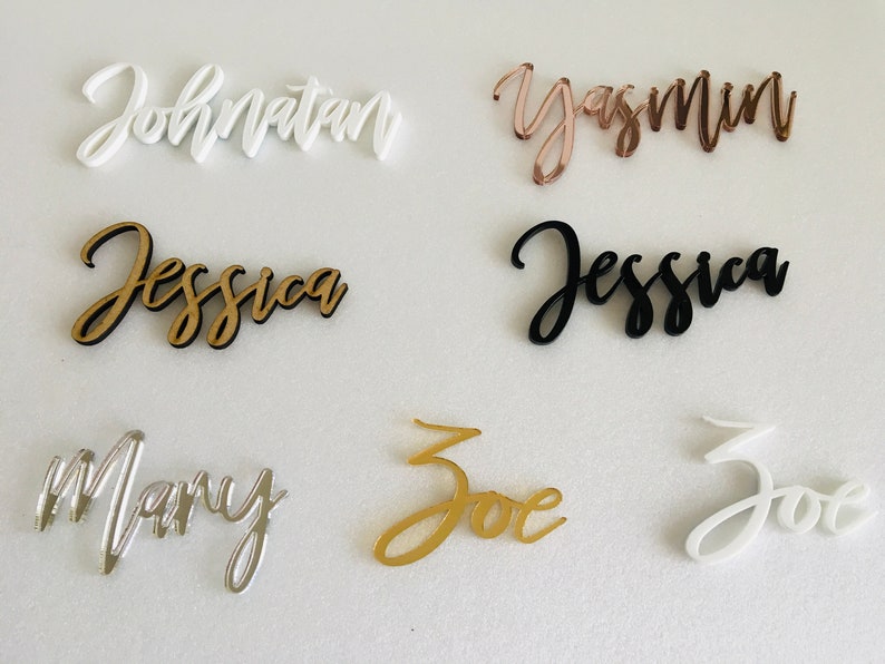 May include: Six acrylic name place cards in various colours, including white, black, gold, silver, and rose gold. The names are written in a cursive font. The names are: Jonathan, Yasmin, Jessica, Mary, Zoe, and Zoe.