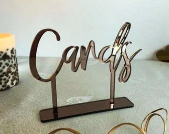 May include: A mirrored acrylic sign with the word "Candies" in a cursive font. The sign is on a stand and has a reflective surface.