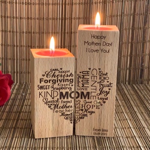 May include: Two wooden candle holders with a red candle in each. The candle holder on the left has a heart-shaped design with words like "Cherish", "Forgiving", "Kind Mom", and "Hope". The candle holder on the right has the text "Happy Mothers Day! I Love You!" and a heart-shaped design with words like "Gentle", "Trust", and "Joy".
