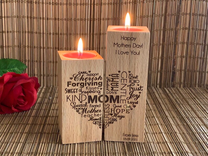 May include: Two wooden candle holders with a red candle in each. The candle holder on the left has a heart-shaped design with words like "Cherish", "Forgiving", "Kind Mom", and "Hope". The candle holder on the right has the text "Happy Mothers Day! I Love You!" and a heart-shaped design with words like "Gentle", "Trust", and "Joy".
