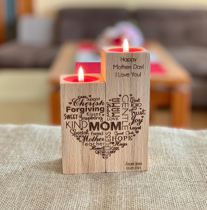 May include: Two wooden candle holders with a heart-shaped design. The candle holders are engraved with words like "Mom", "Love", "Hope", and "Cherish". The text "Happy Mothers Day! I Love You!" is engraved on the top candle holder. The bottom candle holder is engraved with "From Jess 05.09.2021".