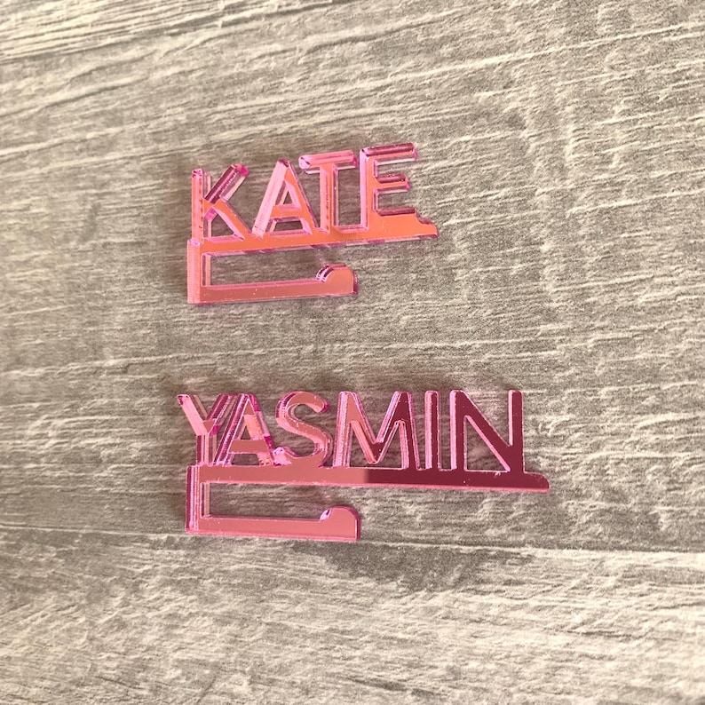 Two pink acrylic nameplates with a hook on the bottom. The top nameplate reads "KATE" and the bottom nameplate reads "YASMIN".