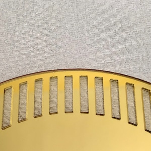 May include: A gold-colored, semi-circular plate with a decorative pattern of evenly spaced rectangular cutouts. The plate has a smooth, shiny surface.