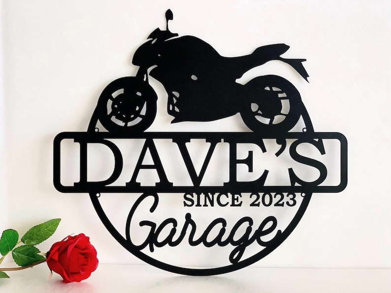 K&ouml;nnte beinhalten: Schwarzes Metallschild mit einer Motorradsilhouette, dem Text "Dave's Garage Since 2023" und einem runden Rand.