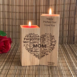 May include: Two wooden candle holders with a heart-shaped design. The left holder has words like "Cherish", "Forgiving", "Kind", and "Mom" engraved on it. The right holder has the words "Happy Mothers Day! I Love You!" engraved on it. The holders are on a wooden surface.