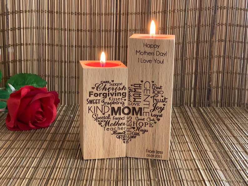 May include: Two wooden candle holders with a heart-shaped design. The left holder has words like "Cherish", "Forgiving", "Kind", and "Mom" engraved on it. The right holder has the words "Happy Mothers Day! I Love You!" engraved on it. The holders are on a wooden surface.