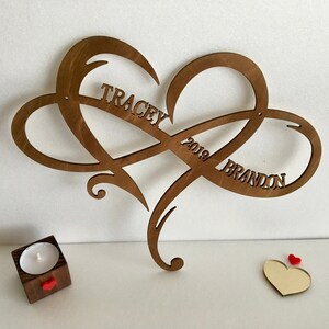 May include: A wooden heart-shaped infinity symbol with the names "Tracey" and "Brandon" and the year "2019" carved into it.