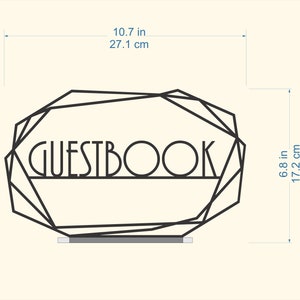 K&ouml;nnte beinhalten: Schwarzer geometrischer Rahmen aus Metall mit dem Wort "GUESTBOOK" in der Mitte. Der Rahmen ist 27,1 cm breit und 17,2 cm hoch.