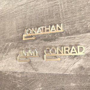Two silver mirror-like nameplates with the names "Jonathan" and "Jimmy Conrad" on them. The nameplates are mounted on a wood surface.