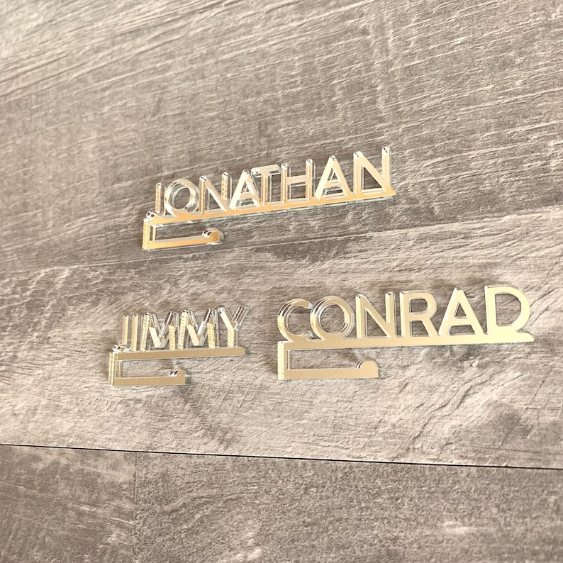 Two silver mirror-like nameplates with the names "Jonathan" and "Jimmy Conrad" on them. The nameplates are mounted on a wood surface.