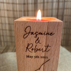 May include: A wooden candle holder with a lit candle inside. The holder is engraved with the names "Jasmine & Robert" and the date "May 5th 2021".