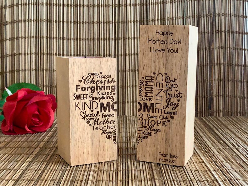 May include: Two wooden blocks with engraved messages. The first block has a candle holder and is engraved with words like "Cherish", "Forgiving", "Kind", and "Mother". The second block is engraved with "Happy Mothers Day! I Love You!" and a list of words like "Trust", "Joy", and "Hope".