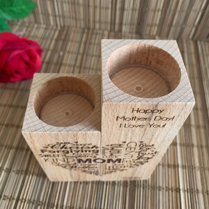 May include: Wooden candle holder with two slots for tealight candles. The holder is engraved with the words "Happy Mothers Day I Love You" and a heart shape filled with words like "caring, forgiving, sweet, trusting, kind, mom".