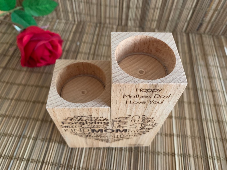 May include: Wooden candle holder with two slots for tealight candles. The holder is engraved with the words "Happy Mothers Day I Love You" and a heart shape filled with words like "caring, forgiving, sweet, trusting, kind, mom".