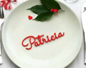 May include: Red plastic name card with the name "Patricia" written in a cursive font. The card is placed on a white plate with a small red heart and green leaves.