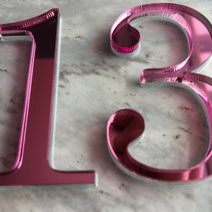 May include: Pink mirrored acrylic number 13. The numbers are thick and have a reflective surface.