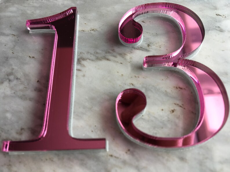 May include: Pink mirrored acrylic number 13. The numbers are thick and have a reflective surface.