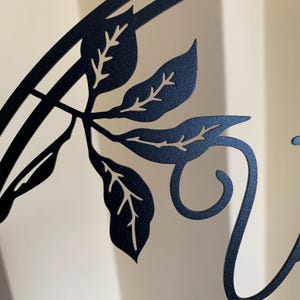 May include: Black metal wall decor with a vine and leaves design. The vine is curled into a decorative swirl.