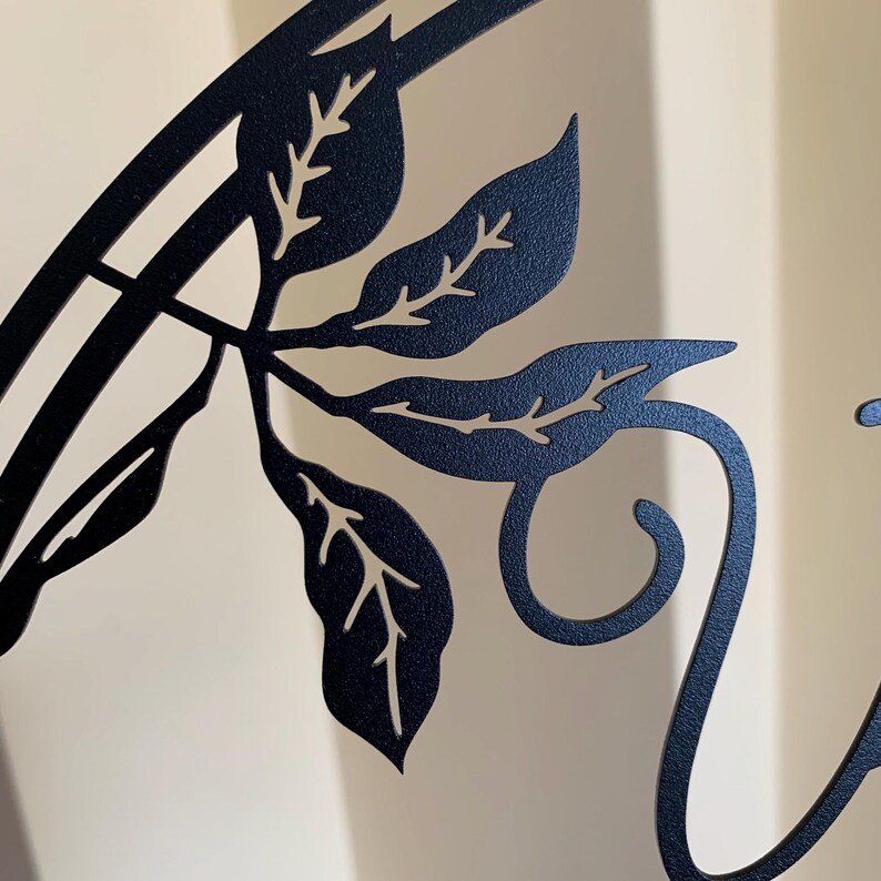 May include: Black metal wall decor with a vine and leaves design. The vine is curled into a decorative swirl.