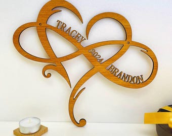 May include: A wooden heart-shaped infinity symbol with the names "Tracey" and "Brandon" and the year "2024" engraved on it.
