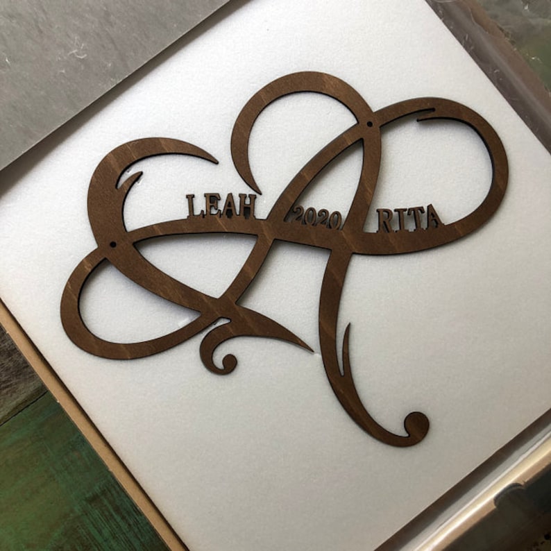 May include: A brown wooden heart-shaped sign with the names "Leah" and "Rita" and the year "2020" inscribed on it.