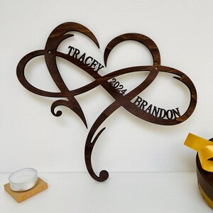 May include: A wooden heart-shaped infinity symbol with the names "Tracey" and "Brandon" and the year "2024" inscribed on it.