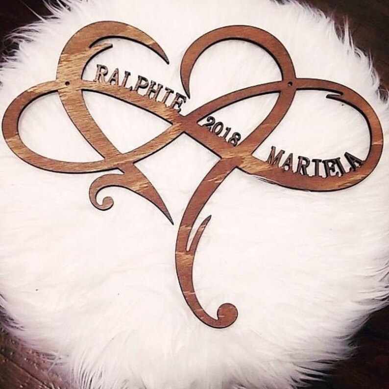 May include: A wooden infinity symbol heart with the names "Ralph" and "Mariela" and the year "2018" carved into it.