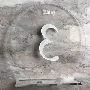 May include: Clear acrylic table number with the number 3 printed in white. The text "TABLE" is printed upside down at the top of the circle.