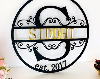 以下が含まれることがあります： 黒い金属製の丸い看板に、金色の「S」の文字と、金色の文字で「SIDDHI」という名前が書かれています。看板には、装飾的なスクロールデザインと「est. 2017」という文字も含まれています。