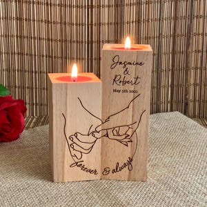 May include: Two wooden candle holders with a design of two hands intertwined. The candle holders are engraved with the text "Jasmine & Robert May 5th 2021 Forever & Always".