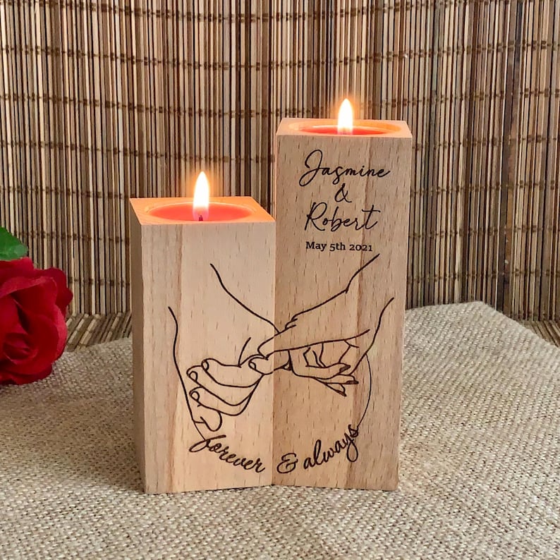 May include: Two wooden candle holders with a design of two hands intertwined. The candle holders are engraved with the text "Jasmine & Robert May 5th 2021 Forever & Always".