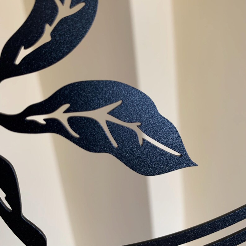 May include: Close-up of a black metal wall decor with a cut-out design of leaves and branches.